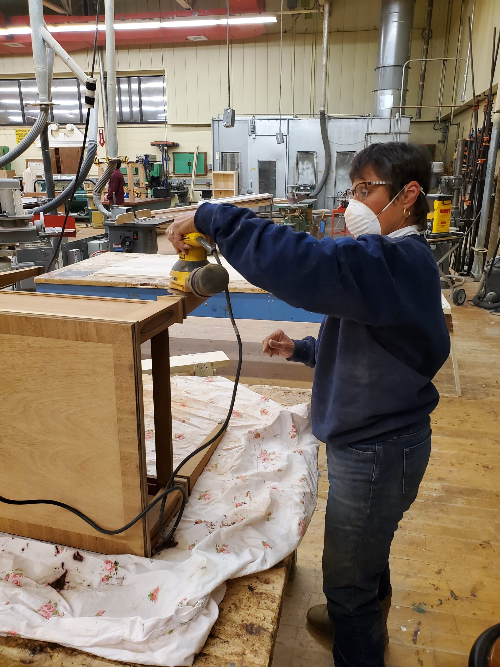 Furniture refinishing woman sands a table with electric hand sander